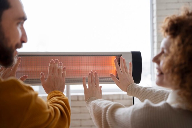 smiley-couple-warming-up-hands-near-heater_23-2149339534